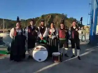 Seis integrantes de la Banda Gaites Candás junto a un puerto