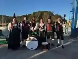 Seis integrantes de la Banda Gaites Candás junto a un puerto